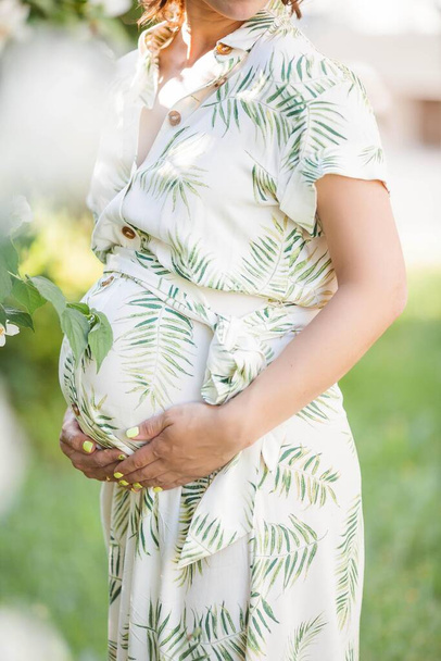 Beautiful young happy pregnant woman is standing near the blossoming tree. Motherhood. Love. Spring. - Zdjęcie, obraz