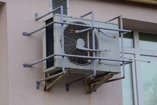 jeden duży szary klimatyzator za żelaznymi kratami na brązowej ścianie budynku z oknem na ulicy - Zdjęcie, obraz
