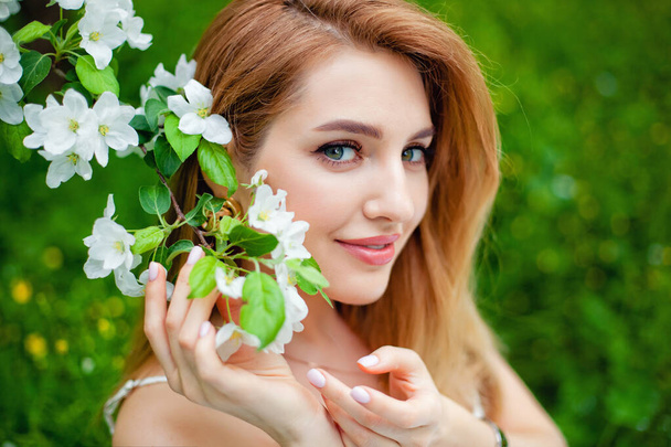 Beautiful teen redhead girl enjoying life in spring blossoming garden against blooming trees. Young dreamy thoughtful lady in nature at sunset. Springtime at countryside concept - Photo, Image