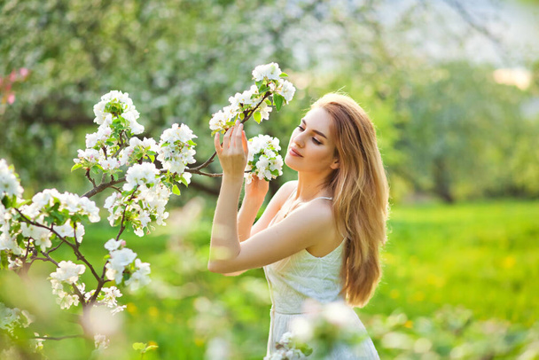 Красивая рыжая девушка-подросток наслаждается жизнью в весеннем цветущем саду против цветущих деревьев. Молодая мечтательная задумчивая леди на природе на закате. Весна в сельской местности - Фото, изображение