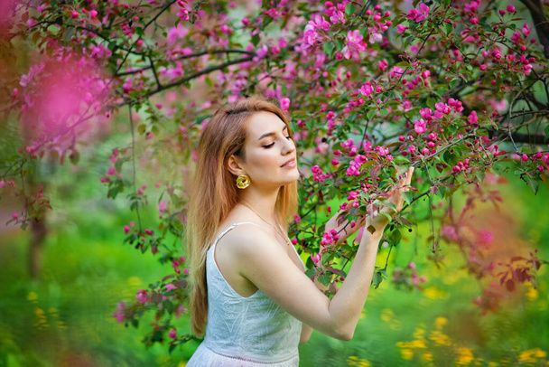 美しい十代の赤毛の女の子は、春の開花庭で花の木に対して人生を楽しんでいます。日没の自然の中で若い夢のような思慮深い女性。田舎のコンセプトで春 - 写真・画像