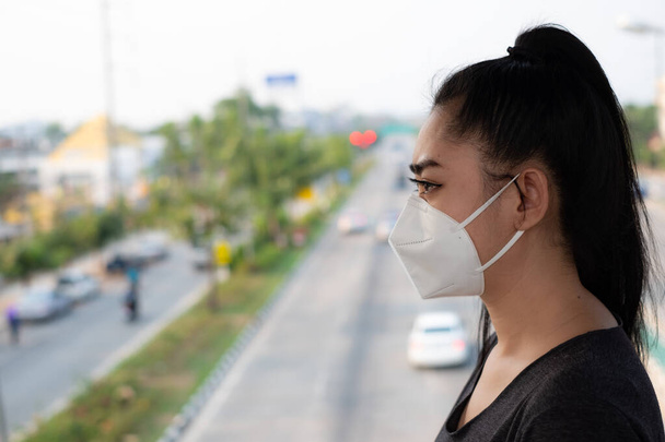 Крупный план женщины, стоящей надеть респиратор N95 маску для защиты от респираторных заболеваний в воздухе, как грипп ковид-19 коронавируса Эбола PM2.5 пыли и смога на дороге зарыли задний план
 - Фото, изображение