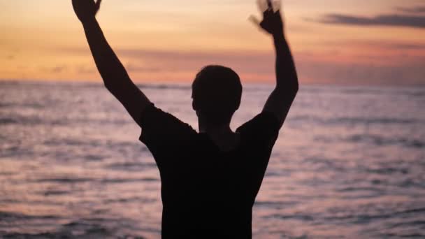 Siluetti mies nostaa kätensä seisomaan kaunis trooppinen ranta punainen auringonlasku. Vapauden käsite
. - Materiaali, video