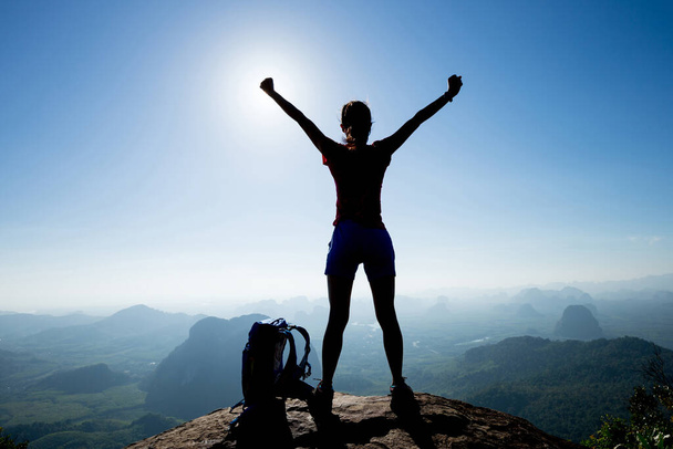 Cheering female backpacker enjoying view on sunrise mountain top cliff edge - Photo, Image