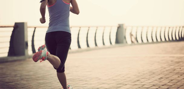 Sportowa biegaczka fitness biegająca po nadmorskiej promenadzie podczas wschodu słońca - Zdjęcie, obraz