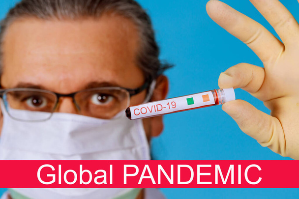 顔のマスクの医師の手のサンプルチューブでのコロナウイルスCOVID-19感染した血液サンプルと世界的なパンデミック - 写真・画像