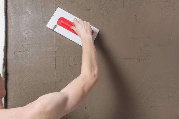 Hand holding a spatula with construction mix.Applying putty or tile glue to the wall.Plaster the wall with a putty knife.Internal construction and finishing works. Repair the wall. Plastering the wall - Photo, Image