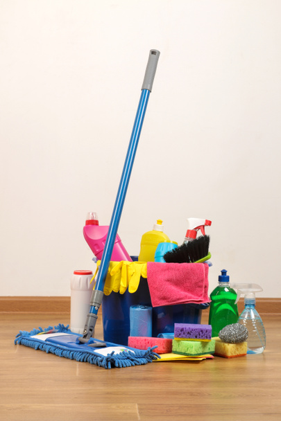 Erilaisia pulloja, joissa on puhdistusaineita ja pesuaineita, pesulappuja sinisessä ämpärissä ja moppi lattialla olevassa huoneessa
 - Valokuva, kuva