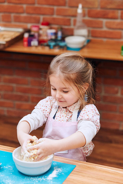Little girl kneading the dough for baking the cake. Kid taking part in baking workshop. Baking classes for children,  aspiring little chefs. Learning to cook. Combining and stirring prepared ingredients. Real people, authentic situations - 写真・画像