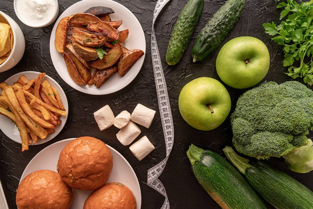Concepto de comida saludable y poco saludable. Frutas y verduras vs dulces y papas fritas vista superior plana yacía con una cinta métrica
 - Foto, imagen