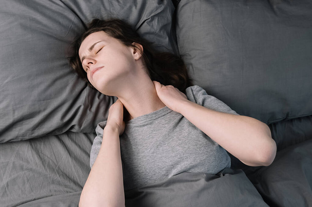 Tired unhappy young woman lying in bed in morning feels pain in neck after night sleep, massage tense neck muscles, exhausted upset girl suffering from shoulder ache. Fibromyalgia concept - Photo, Image