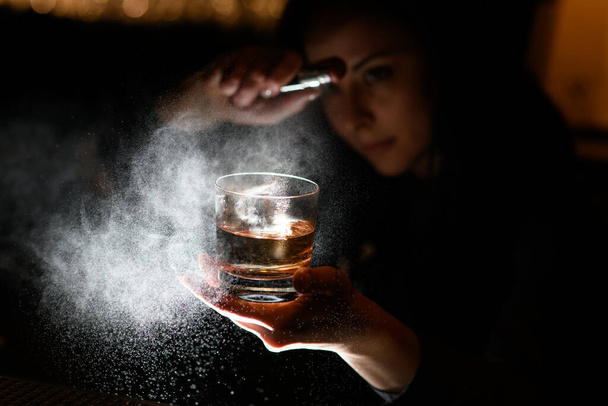 Woman bartender holds in one hand glass with alcoholic drink and sprinkles on it. - Foto, immagini