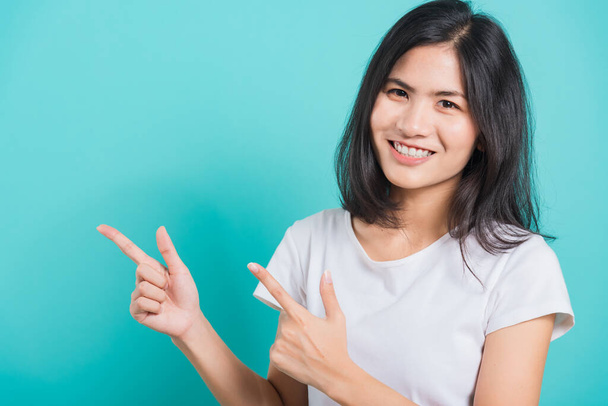 Portrait Asian beautiful young woman wearing white T-shirt standing smile white teeth, She pointing finger up and looking at camera, shoot photo in studio on blue background, There was copy space. - Photo, Image