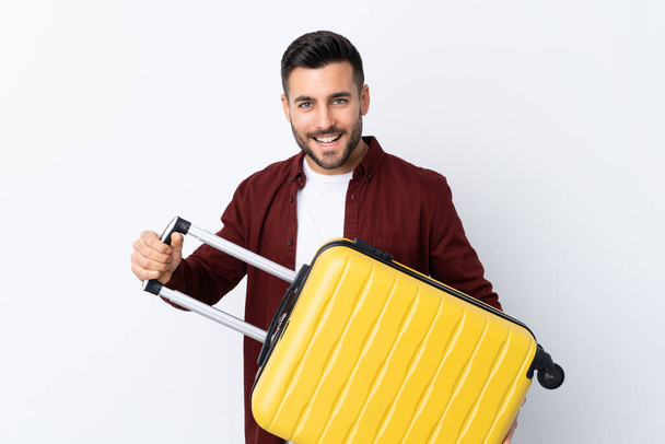 Young handsome man over isolated white background in vacation with travel suitcase - 写真・画像