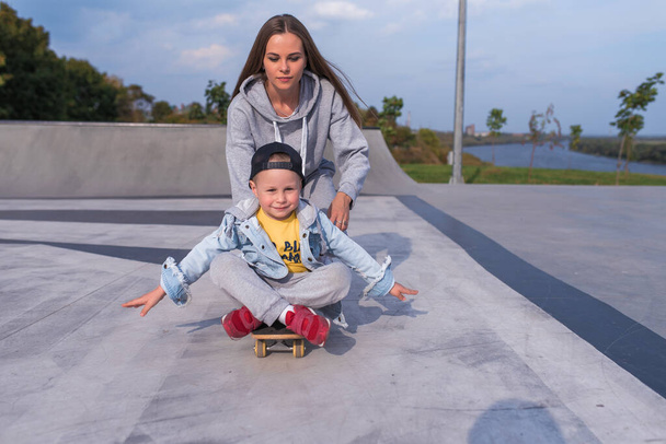 Family woman mom son of boy on skateboard, help support in training sports fitness. Emotions of happiness, fun of relaxation joy, smile laughter. Summer sports ground. Free space for copy text. - Foto, Imagen