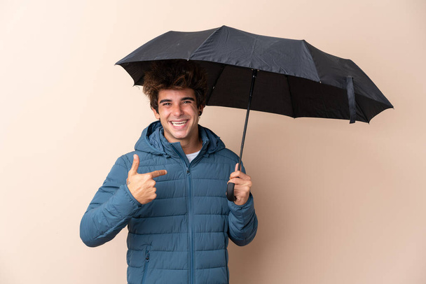 Hombre sosteniendo un paraguas sobre un fondo aislado con expresión facial sorpresa
 - Foto, Imagen