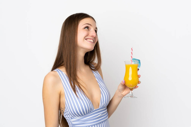 jonge Kaukasische vrouw geïsoleerd op witte achtergrond in badpak en het houden van een cocktail - Foto, afbeelding