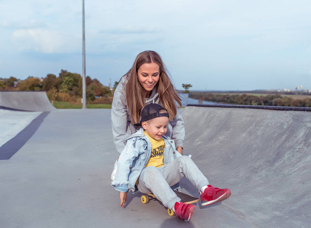 Family woman mom son of boy on skateboard, help support in training sports fitness. Emotions of happiness, fun of relaxation joy, smile laughter. Summer sports ground. Free space copy text. - Foto, Imagem