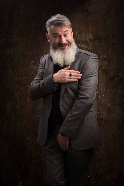 Retrato de un hombre de mediana edad con barba y bigote posando con vestimenta formal sobre un telón de fondo oscuro, enfoque selectivo
 - Foto, Imagen