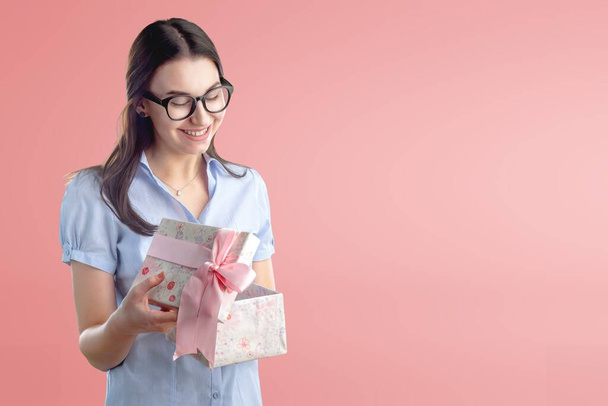 young woman holding a gift box on pink background - Foto, imagen