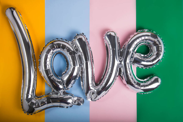 Love word of a silver foil balloon on multicolor background. Happy Valentine's day festival concept. Declaration of different kinds of love. LGBT rights - Foto, immagini