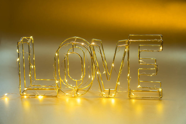 Love concept. Valentine's Day. Wire word LOVE lettering with lighting garland on golden shining holiday background. Copy space - Fotó, kép