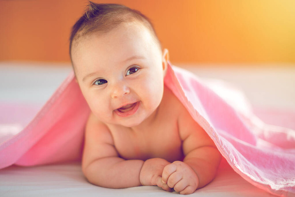 Lindo bebé de tres meses de edad niña en una cama sobre su vientre con la cabeza hacia arriba mirando a la cámara con sus grandes ojos. Luz natural dormitorio
. - Foto, Imagen