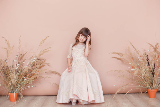 Young model girl in beige dress posing on pastel color background with deadwoods in pot - Photo, Image