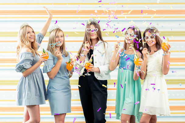 Pretty smiling teenage girls in dresses and crowns holding beverages - 写真・画像