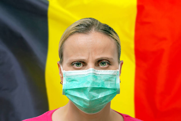 Жінка з маскою дивиться на камеру на задньому плані бельгійського прапора. Концепція уваги до всесвітнього поширення коронавірусу по всьому світу. Коронавірус у Бельгії.. - Фото, зображення