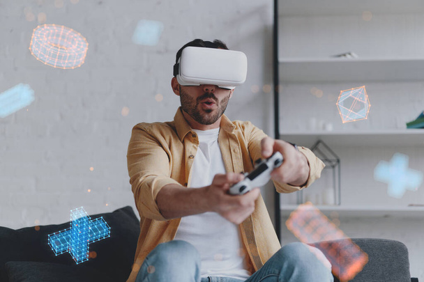 Young smiling man in VR glasses playing game using joystick, augmented reality - Foto, Bild