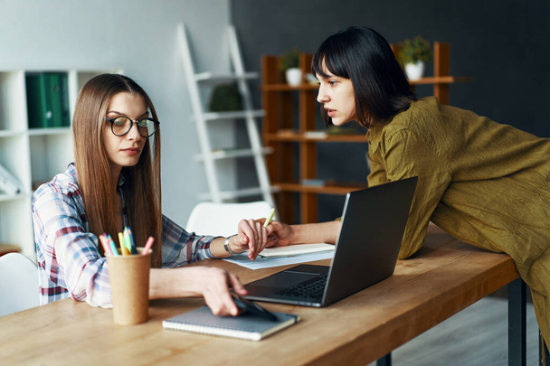 Duas empresárias sérias tendo uma reunião usando laptop no escritório
 - Foto, Imagem