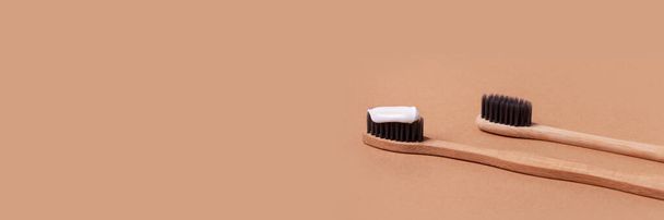 fundo neutro minimalista com duas escovas de dentes de madeira e uma pasta em um deles
 - Foto, Imagem