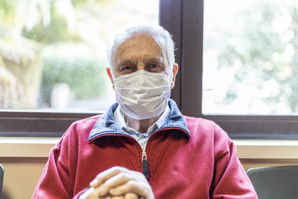 呼吸器のある病院の医師室に座っている老人はカメラを見てください - 写真・画像