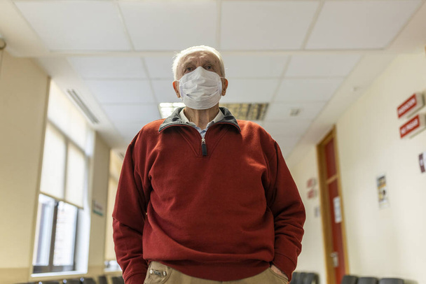 Elderly man walking down a corridor of medical consultation in a hospital with respirator, front view - Photo, Image
