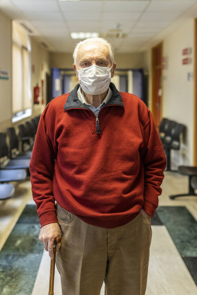 Elderly man walking down a corridor of medical consultation in a hospital with respirator, front view - Photo, Image