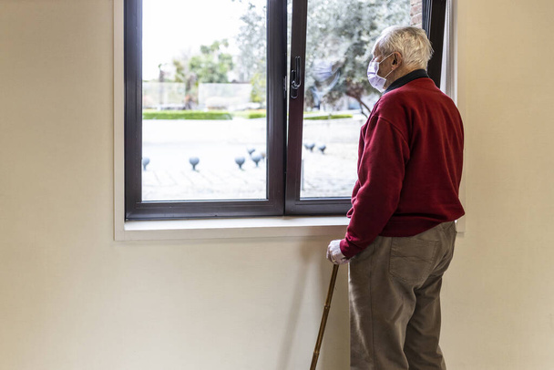 Älterer Mann blickt mit Atemschutzmaske aus dem Fenster der Arztpraxis in einem Krankenhaus. - Foto, Bild