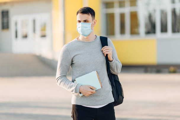 A young man in the background of an open- air building wearing a medical face mask that protects against the spread of coronavirus disease. Close- up of a man with a surgical mask on his face - Foto, Imagem