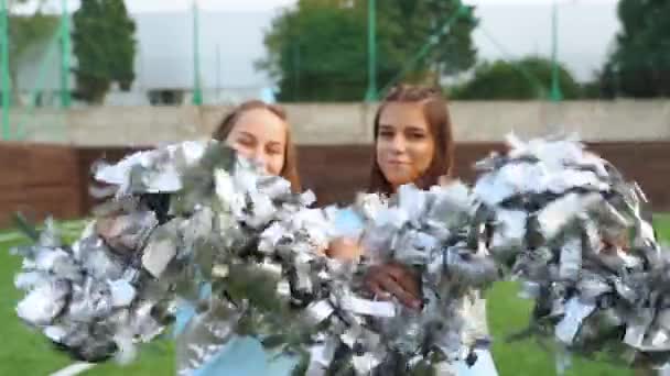 Adolescentes en porristas en uniforme sacudido con pompones, apoyo equipo deportivo universitario
 - Metraje, vídeo