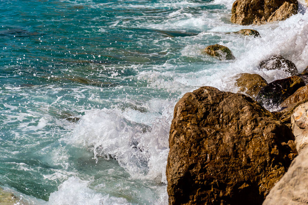 Ένα κοντινό πλάνο με τα γαλαζοπράσινα νερά της Μεσογείου και τα ισχυρά κύματα να χτυπούν στα βράχια της ακτής - Φωτογραφία, εικόνα