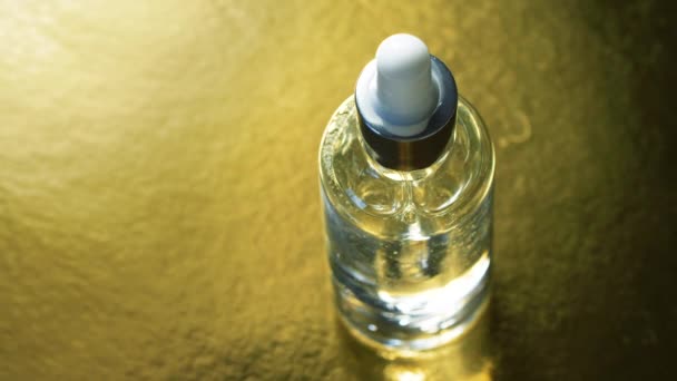 Close up de garrafa de soro de vidro cristal com pipeta dentro girando sobre a superfície de textura de ouro. 4k gel de cuidados cosméticos da pele. Serviços de saúde
. - Filmagem, Vídeo