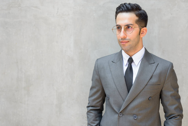 Porträt eines jungen, gut aussehenden persischen Geschäftsmannes im Anzug gegen Betonwand im Freien - Foto, Bild