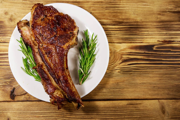 牛の肋骨の目のステーキの骨の上にローズマリーと木製のテーブルの上に白いプレート - 写真・画像