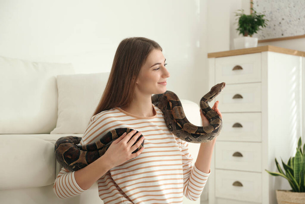 Young woman with boa constrictor at home. Exotic pet - Fotoğraf, Görsel