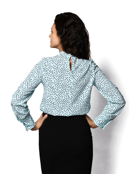 Young beautiful brunette businesswoman in formal office clothing polka dot blouse and pencil skirt has her back to us - Foto, Imagem