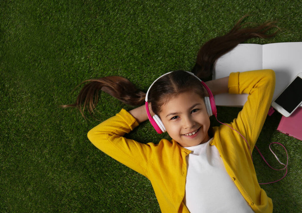 Cute little girl listening to audiobook on grass, top view - Fotó, kép