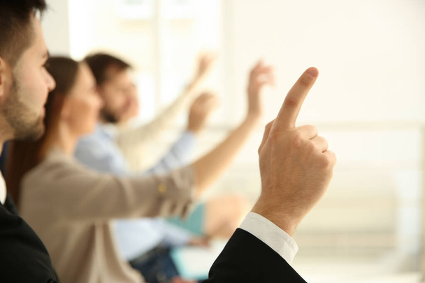 Young man raising hand to ask question at business training indoors, closeup - Foto, Bild