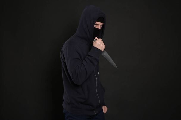 Man in mask with knife on black background. Dangerous criminal - Photo, Image