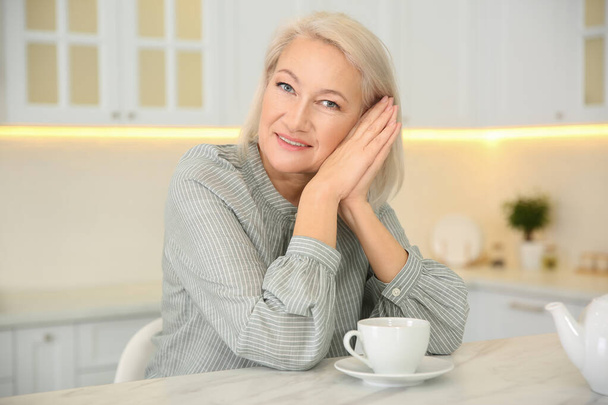 Beautiful mature woman with cup of coffee in kitchen - Foto, imagen