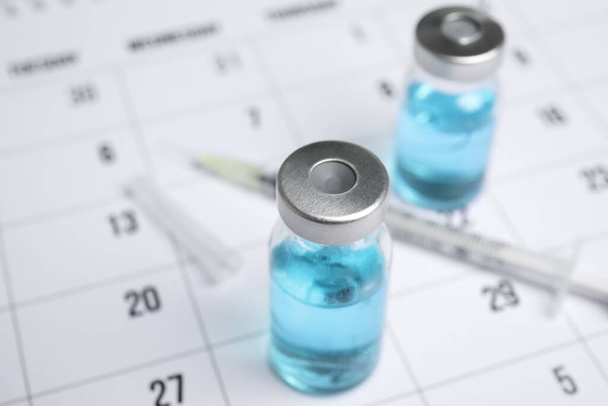 Vial and syringe on calendar, closeup. Vaccination and immunization - Фото, зображення